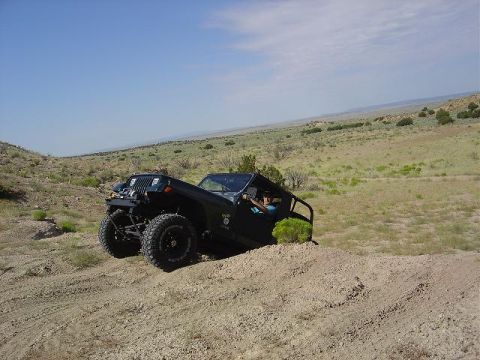 1986 Ford Bronco II - A black off-road vehicle navigates a sandy incline under a clear blue sky.