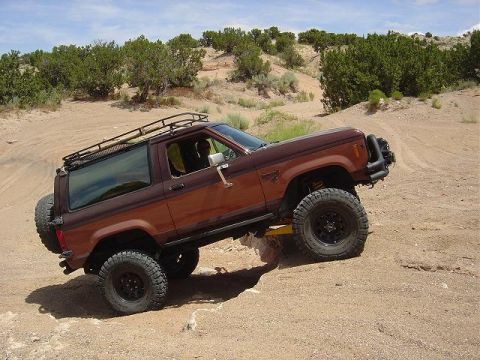1986 Ford Bronco II - This 1986 Ford Bronco II is navigating a challenging off-road trail with steep inclines and sandy terrain.