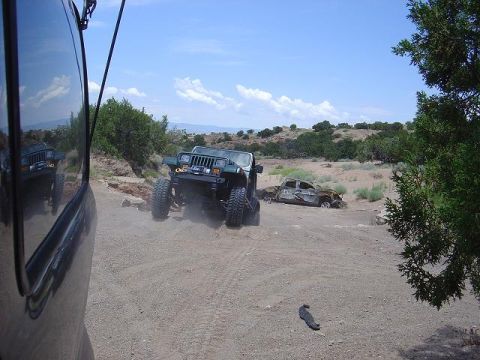 1986 Ford Bronco II - Two vehicles are present in a dusty, arid landscape under a blue sky with scattered clouds.