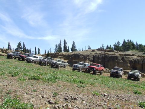 1979 Ford Bronco - A group of Ford Broncos and trucks are parked on a hillside under a partly cloudy sky.