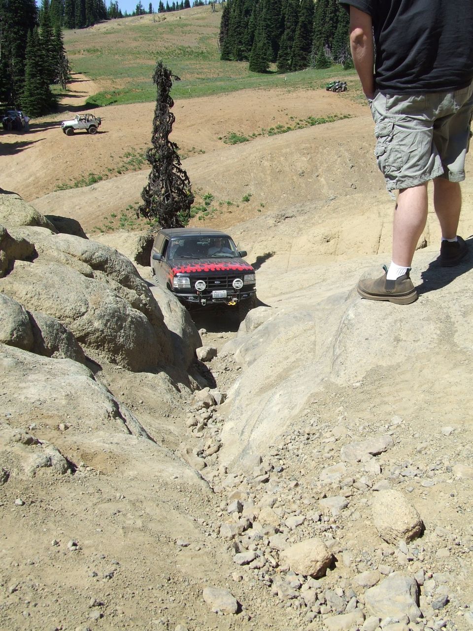 Red and black SUV navigating a rocky off-road trail, with a white SUV in the background