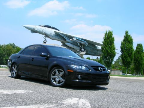 1994 Ford Probe - Black Mazda 6 sedan parked outdoors with a fighter jet in the background.