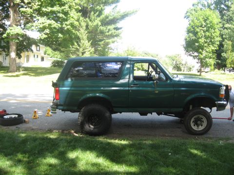 1996 Ford Bronco - A green 1996 Ford Bronco is shown with a suspension lift kit, parked on the side of the road.