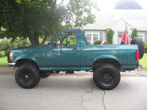 1996 Ford Bronco - Side view of a lifted green 1996 Ford Bronco with off-road tires and a spare tire mounted on the back.
