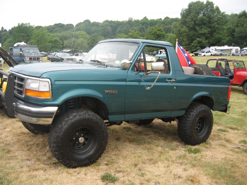 Lifted teal Ford Bronco XL, top removed, side view on grass at a 4x4 show