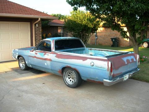 1973 Ford Ranchero - A vintage Ford Ranchero car-based pickup shown from a rear three-quarter angle in a driveway, wearing patchy primer, faded blue paint, and…