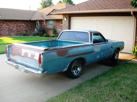 1973 Ford Ranchero - A rear three-quarter view of a vintage Ford Ranchero car-based pickup finished in faded blue paint with extensive surface rust and primer p…