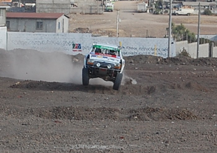 Off-road race truck mid-air, front view. White with green and red accents