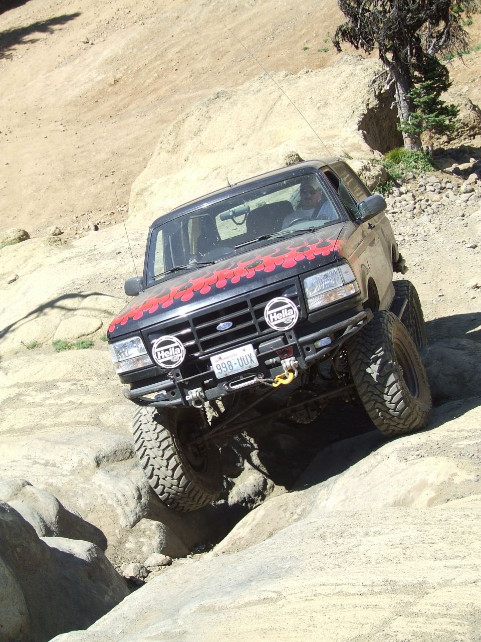 Black Ford Bronco with red flame decals on the hood, lifted suspension, and off-road tires navigating a rocky trail