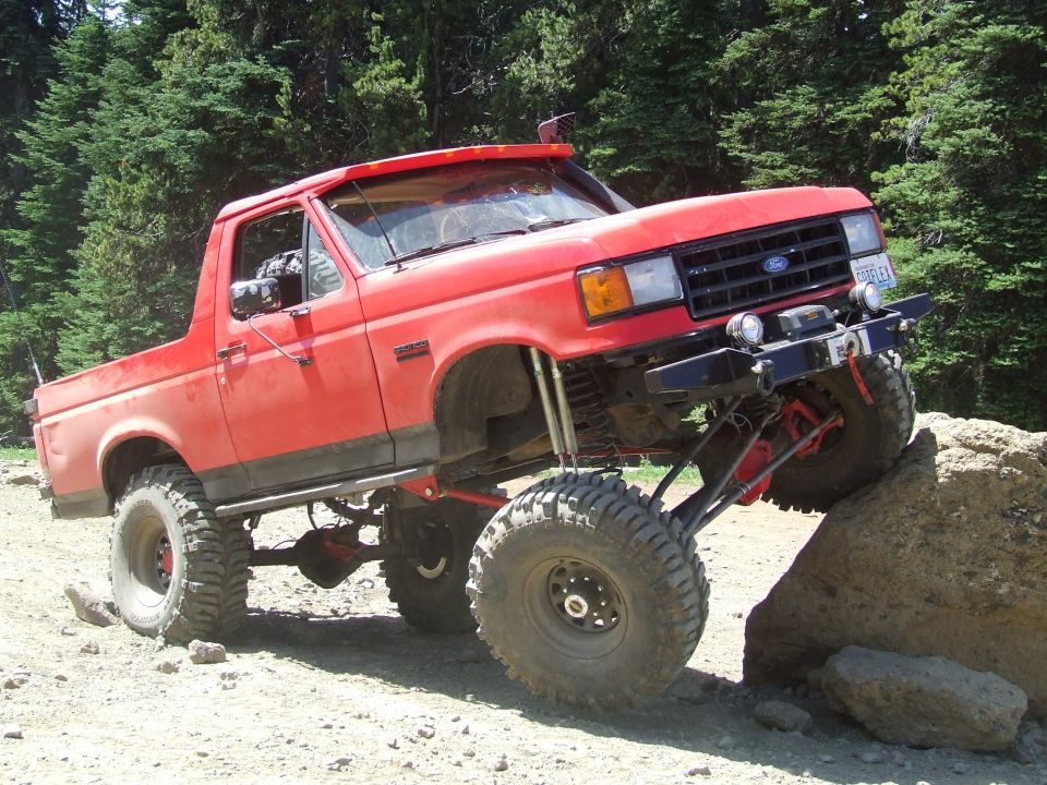 Red lifted 1987 Ford Bronco off-roading on a rock