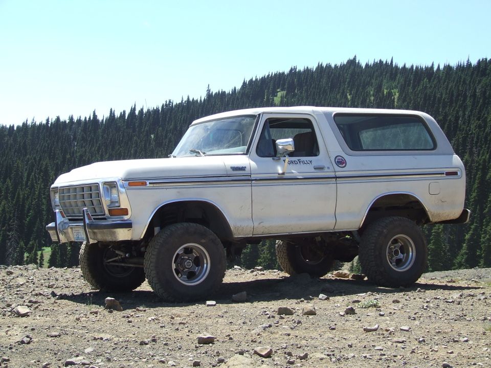 White 1978 Ford Bronco with lifted suspension and off-road tires parked on a rocky incline