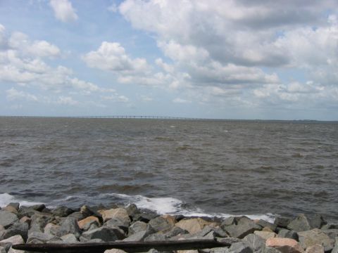 1985 Ford LTD Crown Victoria - A wide expanse of water under a cloudy sky, with a distant bridge stretching across the horizon.