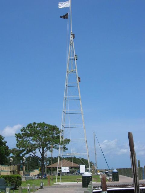1985 Ford LTD Crown Victoria - A tall radio tower stands against a clear blue sky, with flags flying at its peak.