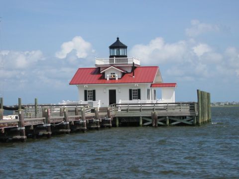 1985 Ford LTD Crown Victoria - A lighthouse stands on a pier, surrounded by the ocean under a partly cloudy sky.