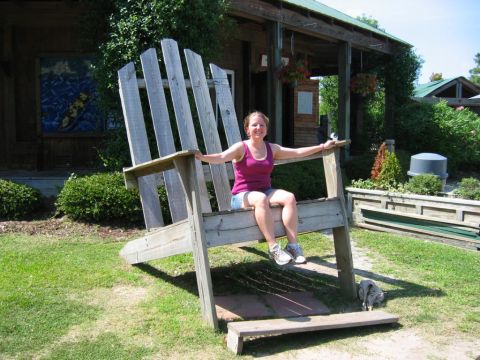 1985 Ford LTD Crown Victoria - A woman poses for a photo while sitting on an oversized wooden Adirondack chair outdoors.