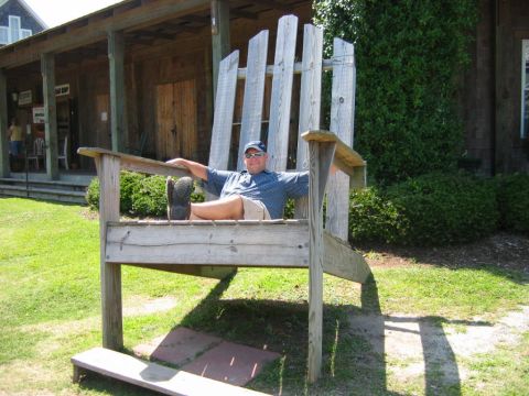 1985 Ford LTD Crown Victoria - A man relaxes in an oversized Adirondack chair on a sunny day.