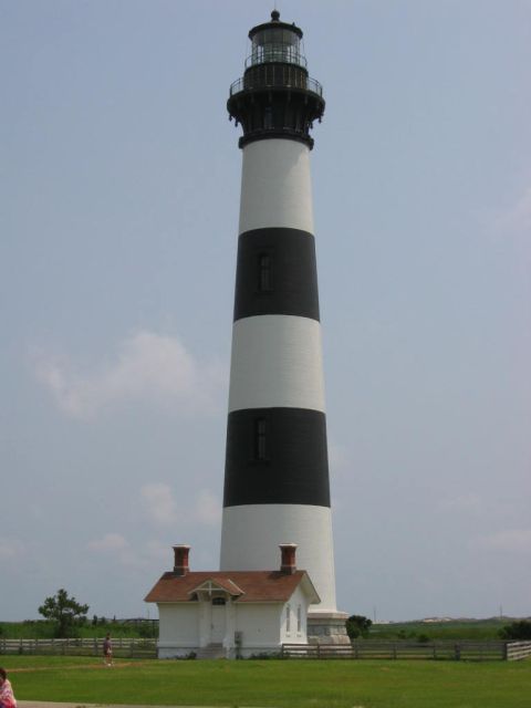 1985 Ford LTD Crown Victoria - A tall lighthouse with black and white bands stands next to a small keeper's house under a cloudy sky.