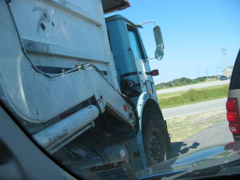 1985 Ford LTD Crown Victoria - A large garbage truck is parked on the side of a road, with another vehicle visible in the foreground.