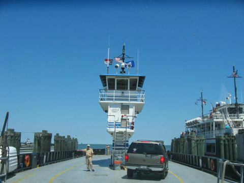 1985 Ford LTD Crown Victoria - A ferry transports vehicles across the water under a clear blue sky.