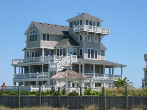 1985 Ford LTD Crown Victoria - A multi-story beach house with numerous balconies and a gazebo stands under a clear blue sky.