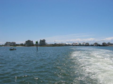 1985 Ford LTD Crown Victoria - A view of a coastal town from the water, showing houses and a small boat on a sunny day.