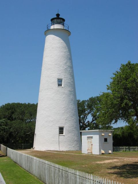 1985 Ford LTD Crown Victoria - The Ocracoke Lighthouse stands tall against a clear blue sky, with lush green trees in the background.