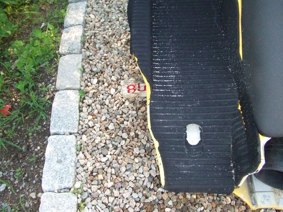Black ribbed rubber traction mat on yellow hull resting on gravel beside cobblestone edging