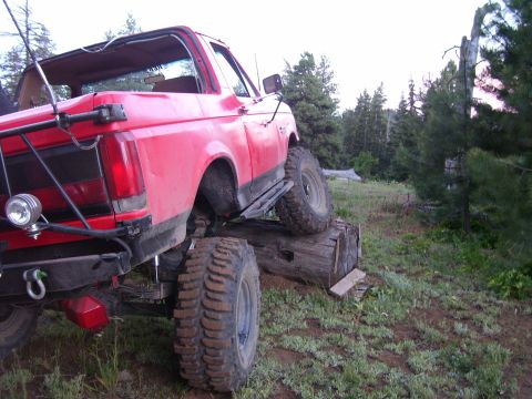 1989 Ford Bronco - This red SUV is positioned on logs, its off-road capabilities in a wooded area.