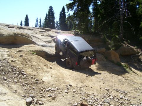 1989 Ford Bronco - A black SUV navigates a steep, rocky off-road trail under a clear blue sky.