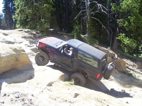 1989 Ford Bronco - This black SUV, modified for off-roading, navigates a challenging rocky terrain.