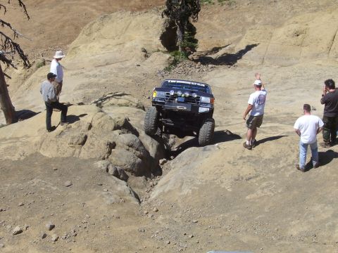 1989 Ford Bronco - A modified truck navigates a challenging rocky obstacle with onlookers observing the maneuver.