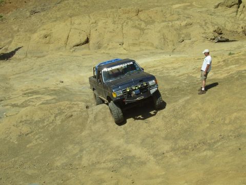 1989 Ford Bronco - A modified pickup truck navigates a challenging off-road course with a spectator observing the action.