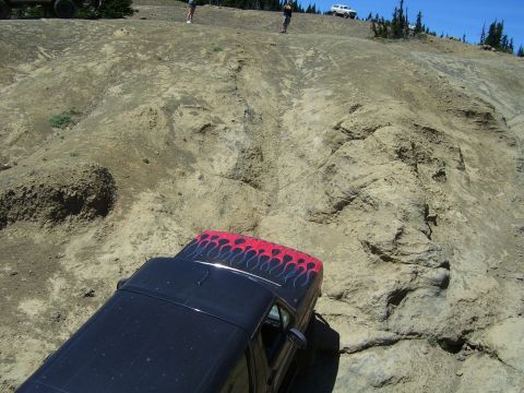 1989 Ford Bronco - A black SUV with custom flame decals navigates a steep, rocky incline, with other vehicles and people visible on the ridge above.