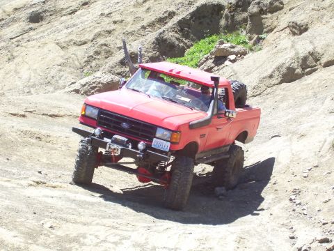 1989 Ford Bronco - This modified pickup truck navigates a steep, rocky incline on a sunny day.