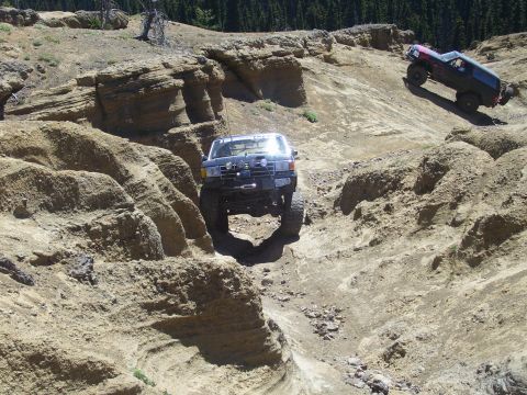 1989 Ford Bronco - Two modified SUVs navigate a challenging off-road trail with steep, eroded terrain.