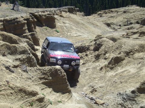 1989 Ford Bronco - This SUV, likely a 1992 Ford Bronco, navigates a challenging off-road course in a rocky, mountainous terrain.