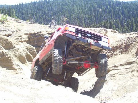 1989 Ford Bronco - A red Ford Bronco navigates a steep, rocky trail with a forest in the background.