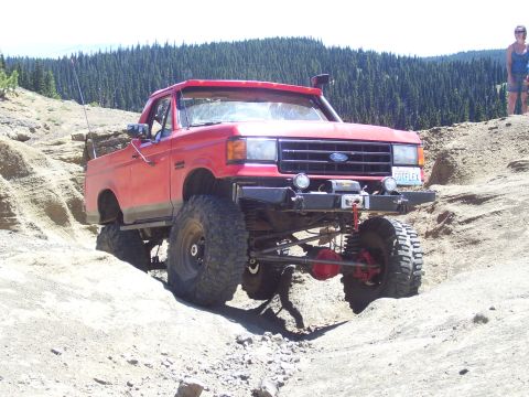 1989 Ford Bronco - Modified red Ford truck with off-road tires tackles a steep, sandy incline on a mountain trail.