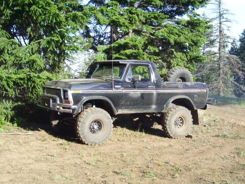 1989 Ford Bronco - A lifted black Ford Bronco sits off-road, surrounded by trees.