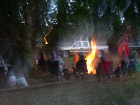 1989 Ford Bronco - A group of people enjoy a campfire in a wooded area, with trucks parked nearby.