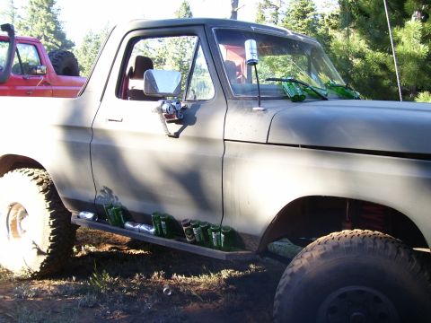 1989 Ford Bronco - A gray Ford Bronco is parked outdoors next to a red truck, with bottles visible on its running board and hood.