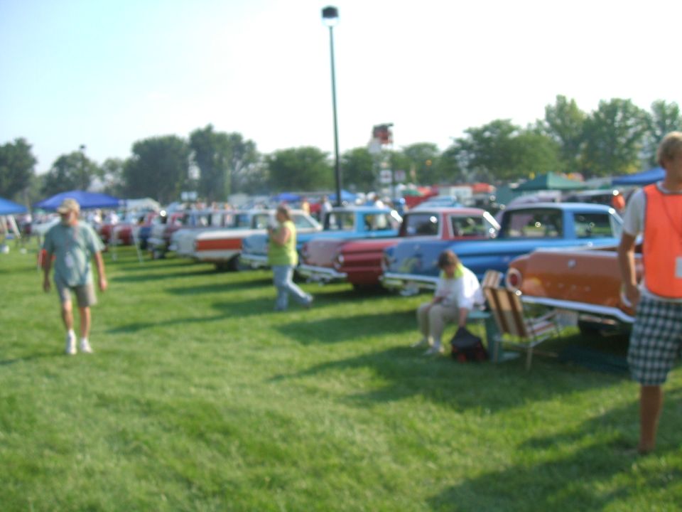 Several cars parked on grass at an outdoor event, with people walking around