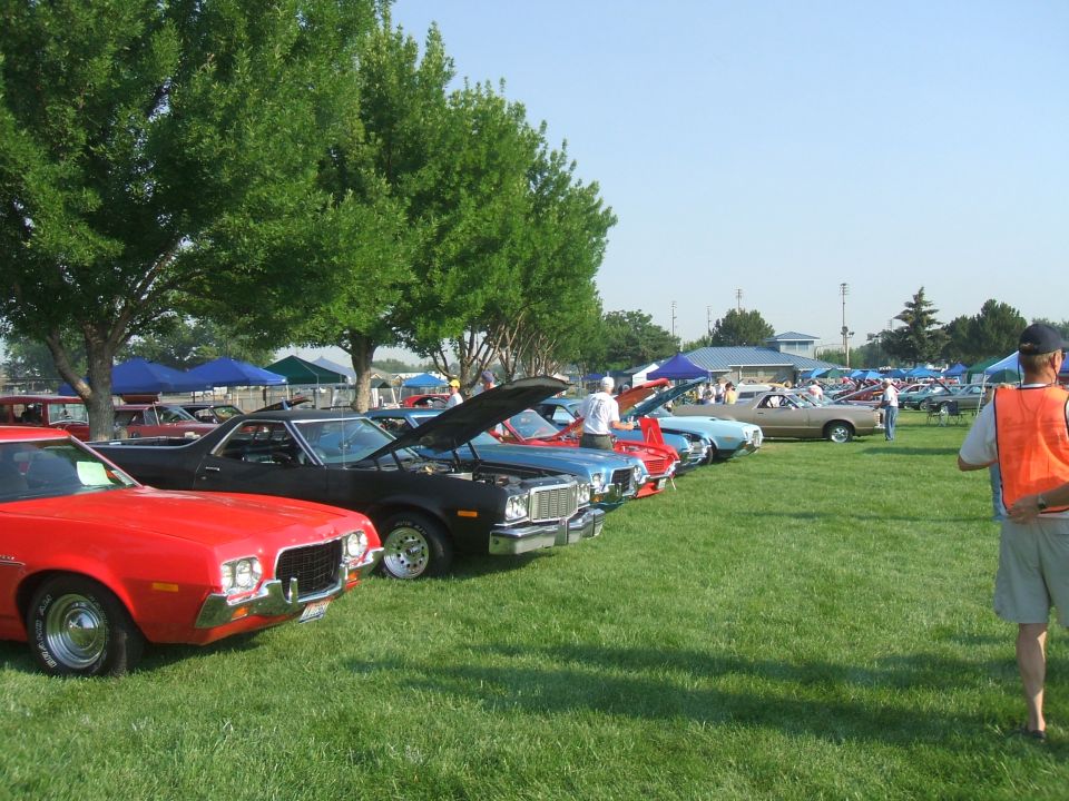 Red 1974 Ford Ranchero in foreground, followed by a line of cars at a show