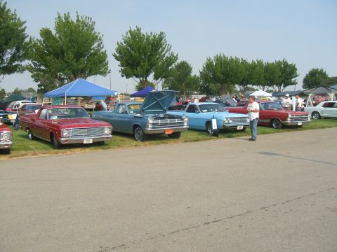 1974 Ford Ranchero - A lineup of vintage vehicles are displayed outdoors under a clear sky, with trees and tents in the background.