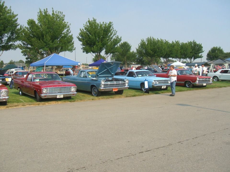 Several classic cars and pickup trucks lined up at an outdoor event. A red pickup is in the foreground