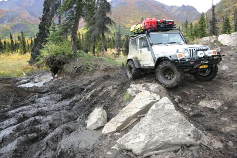 2003 Jeep TJ - A 2003 Jeep TJ tackles a challenging muddy and rocky off-road trail in a mountainous, wooded area.