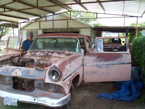 1955 Ford Customline - A man stands by a rusty 1955 Ford Customline sedan, with a truck visible behind it.