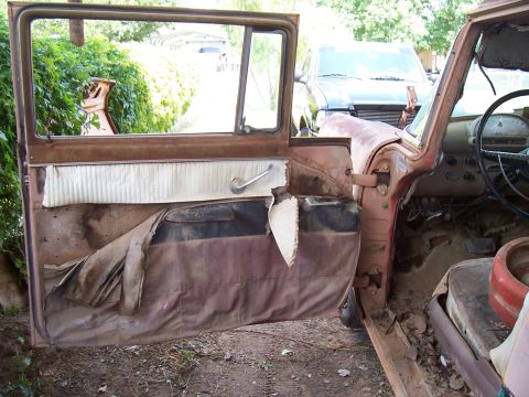 1955 Ford Customline - The interior of a 1955 Ford Customline shows significant wear and tear, with the driver's side door ajar.