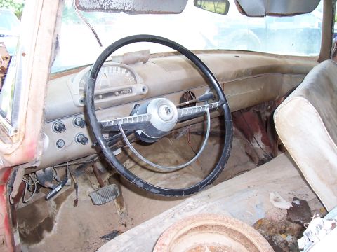 1955 Ford Customline - The interior of a 1955 Ford Customline is visible, a dusty dashboard and steering wheel.
