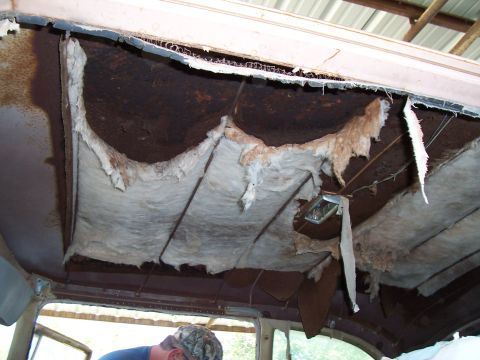 1955 Ford Customline - The interior of a vehicle shows significant damage to the headliner, revealing rust and insulation.